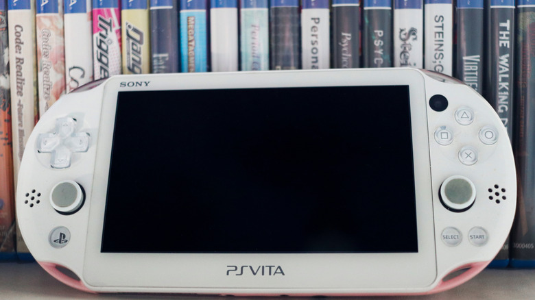 A PS Vita handheld console standing in front of several game boxes.