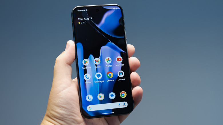 A person holding a Pixel phone displaying the standard Android 14 home screen with fixed Google widgets.
