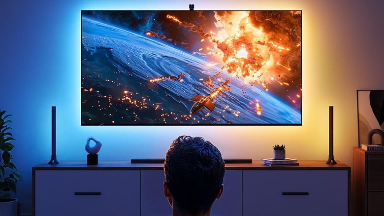 A wall-mounted TV glowing with colorful ambient light that matches the screen content.