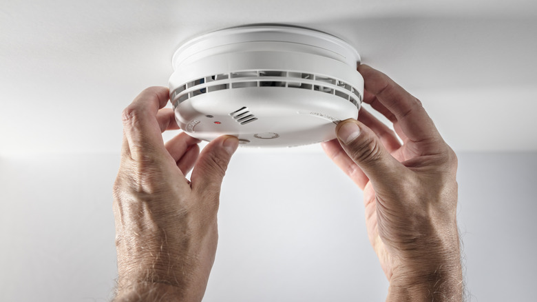 A white smoke detector being installed on a ceiling.