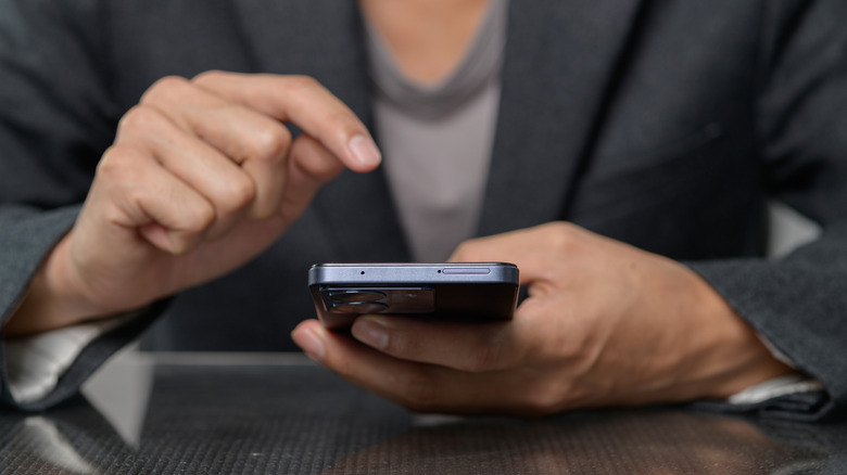A person holding their smartphone with their finger hovering above the display, ready to tap the screen.