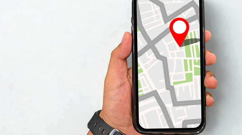 Hand holding a smartphone displaying a map and a red location marker representing real-time positioning.