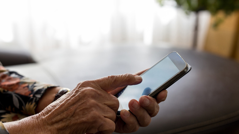 A close-up shot of an older person's finger interacting with a bright smartphone screen.