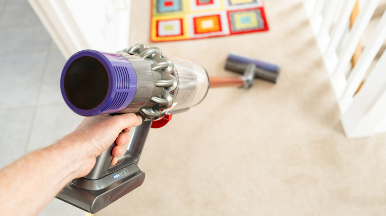 A cordless stick vacuum being used on a carpeted hallway.