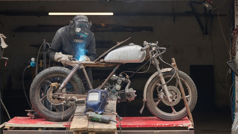 A man welding a custom motorcycle frame in a workshop.