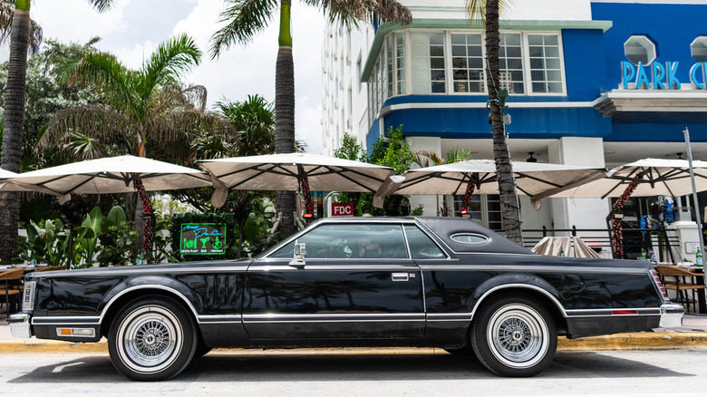 A black Mark V Lincoln Continental luxury coupe parked in front of a blue building.