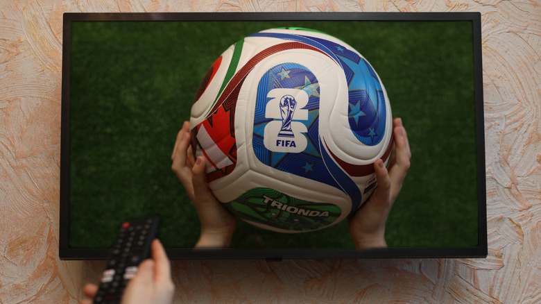 An individual using a remote control while watching a sports match on a bright TV screen.