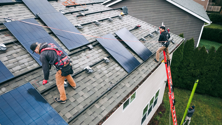 Two professional workers in safety gear installing photovoltaic panels on a house roof.