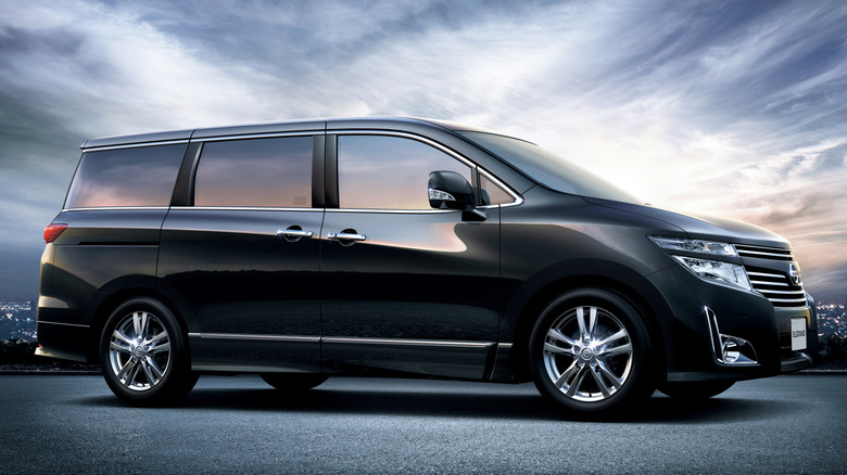 A black Nissan Elgrand parked at night with blurred city lights in the background.
