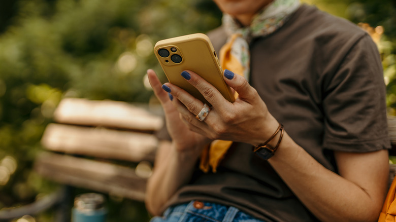 A woman sitting on a park bench focused on her smartphone screen.