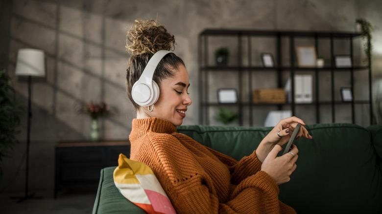 A person smiling while listening to music through headphones connected to their phone.