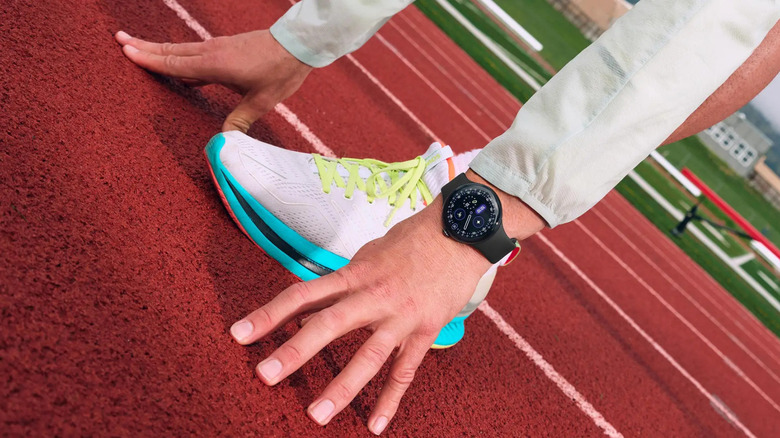 A runner wearing a Google Pixel Watch at the starting line of a track.