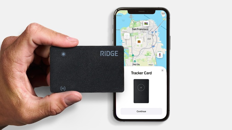 A close-up of a hand holding a slim Ridge Wallet Tracker Card alongside an iPhone.