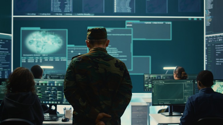 Uniformed military officials and tech experts working in a high-tech digital command center with data displays.