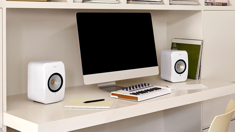 Two teal KEF LSX II wireless speakers arranged on a desk