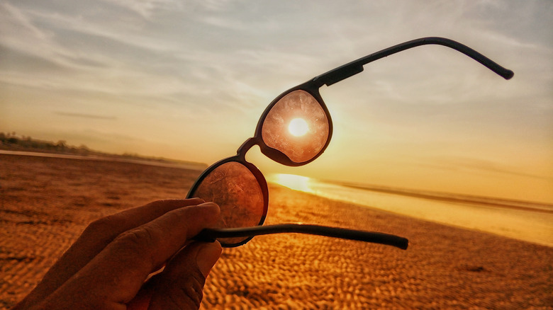 A pair of sunglasses held up against the bright sun.