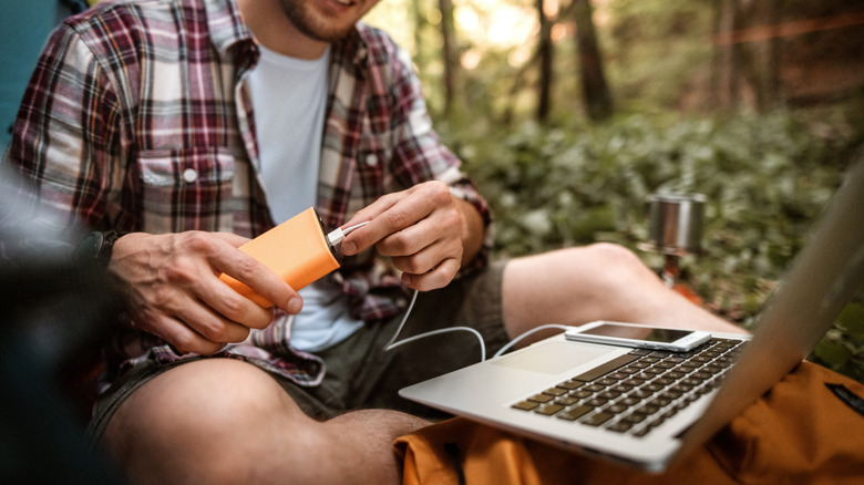 A person in an outdoor tent connecting a laptop to a portable power bank.